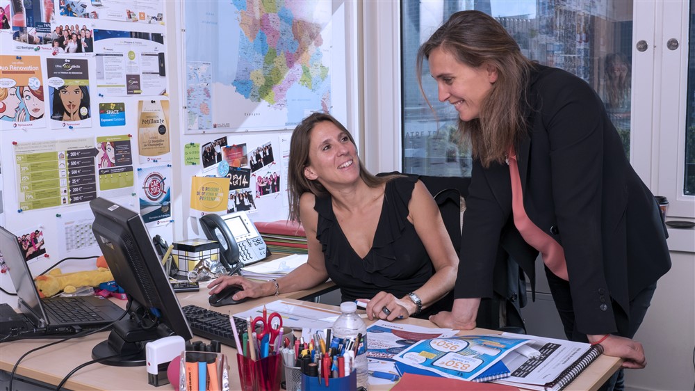 Deux femmes souriantes en train de travailler derrière un bureau