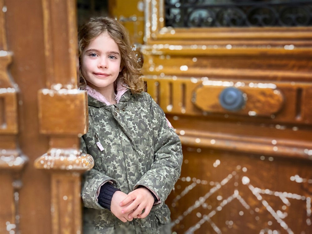 Petite fille posant devant l'objectif devant une porte d'entrée en plein hiver