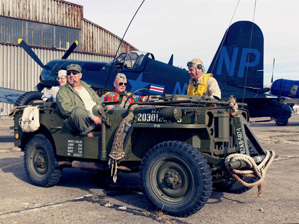 Quatre vétérans sur un quad militaire, en fond un avion militaire bleu sur une piste d'atterrissage