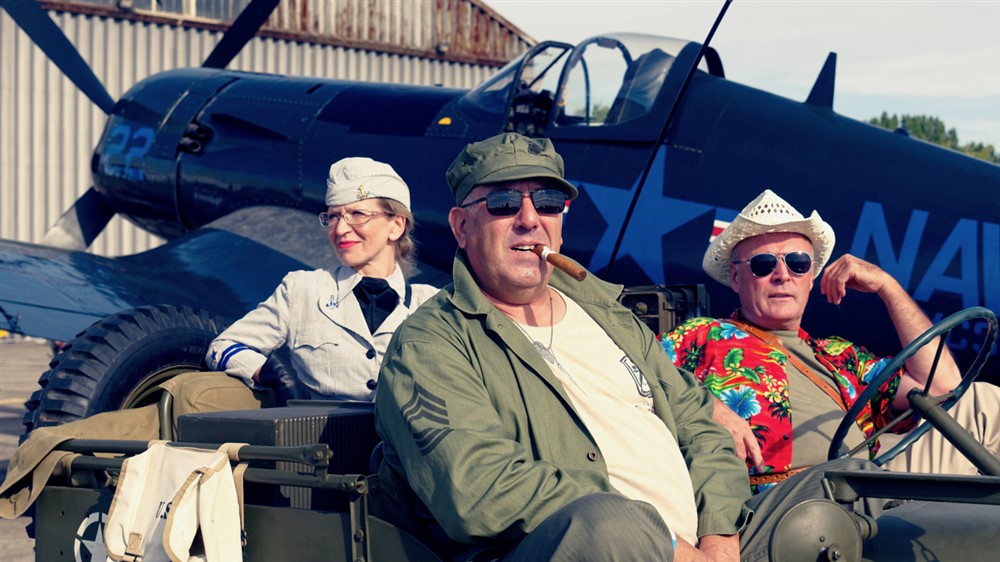 Trois vétérans posant devant l'objectif avec un avion militaire en fond